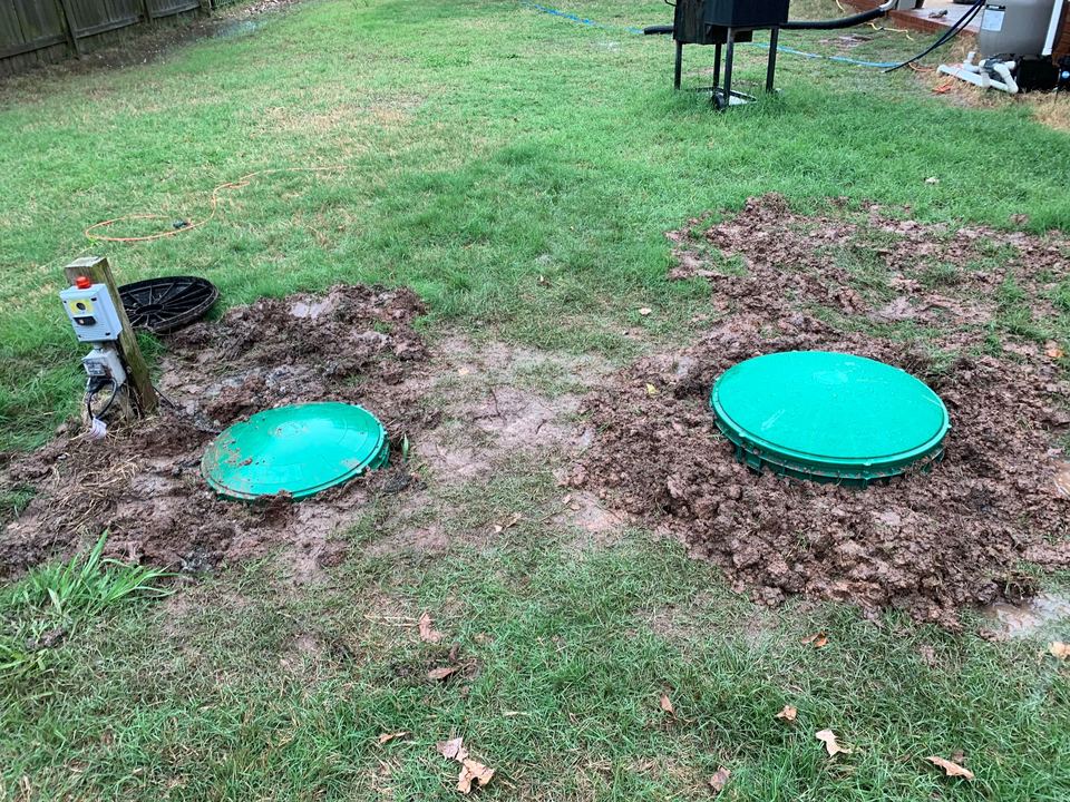 Two septic tank riser lids set at ground level in a back yard